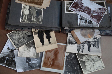 An open photo album and a scattering of loose black&white and sepia-toned photographs, mostly portraits and groups of people, that appear to be from the first half of the 20th century. No faces can be fully seen
