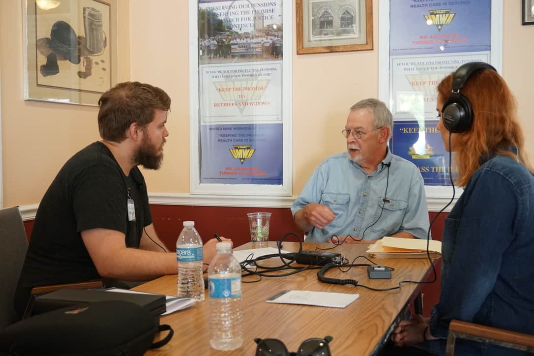 Three people sit at a table, two of them are interviewing the third.