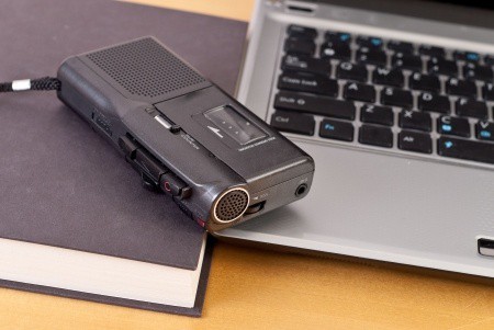 An audio recorder, a laptop, and a book with a black cover