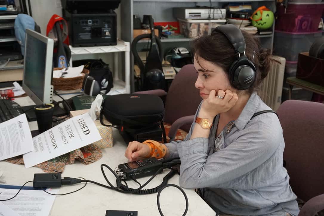 A woman in an office wearing headphones attached to an audio recorder