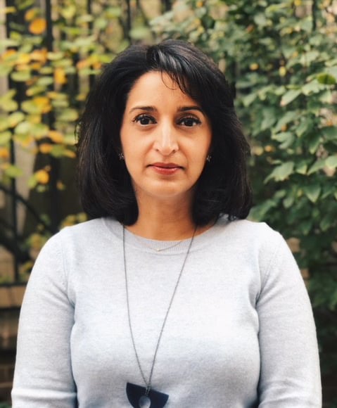 A headshot of a woman, wearing a light gray top, looking into the camera.