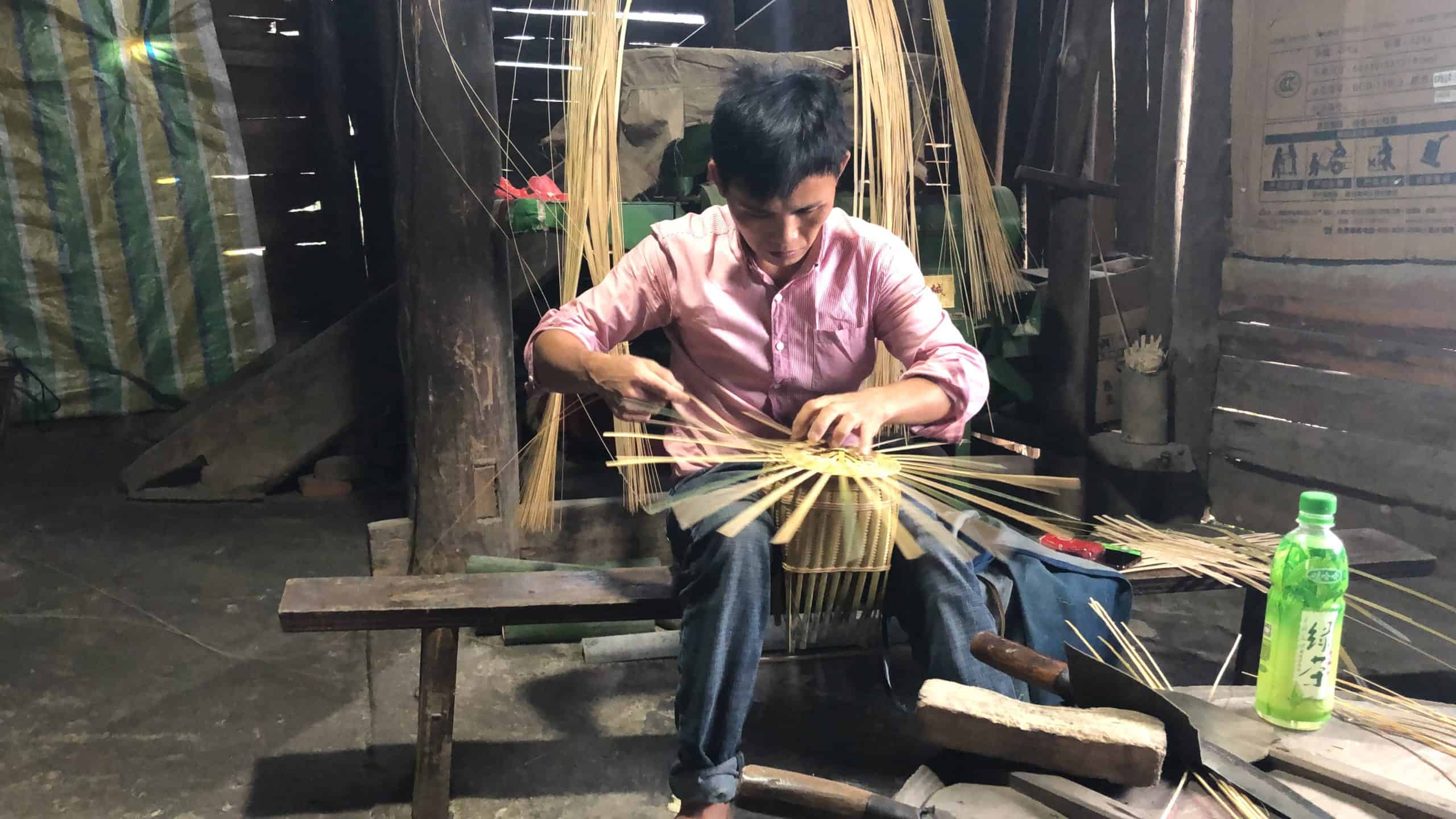 A man sitting on a bench making a basket from cane splits..