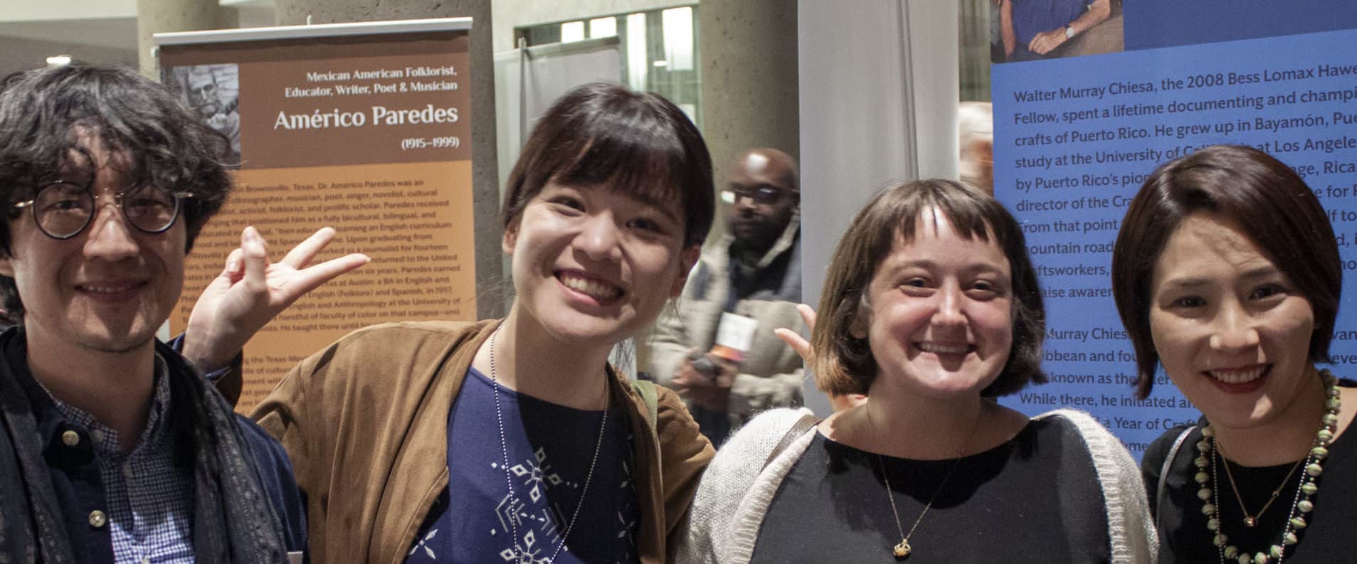 Four individuals pose for the camera in front of some banners at a professional conference.