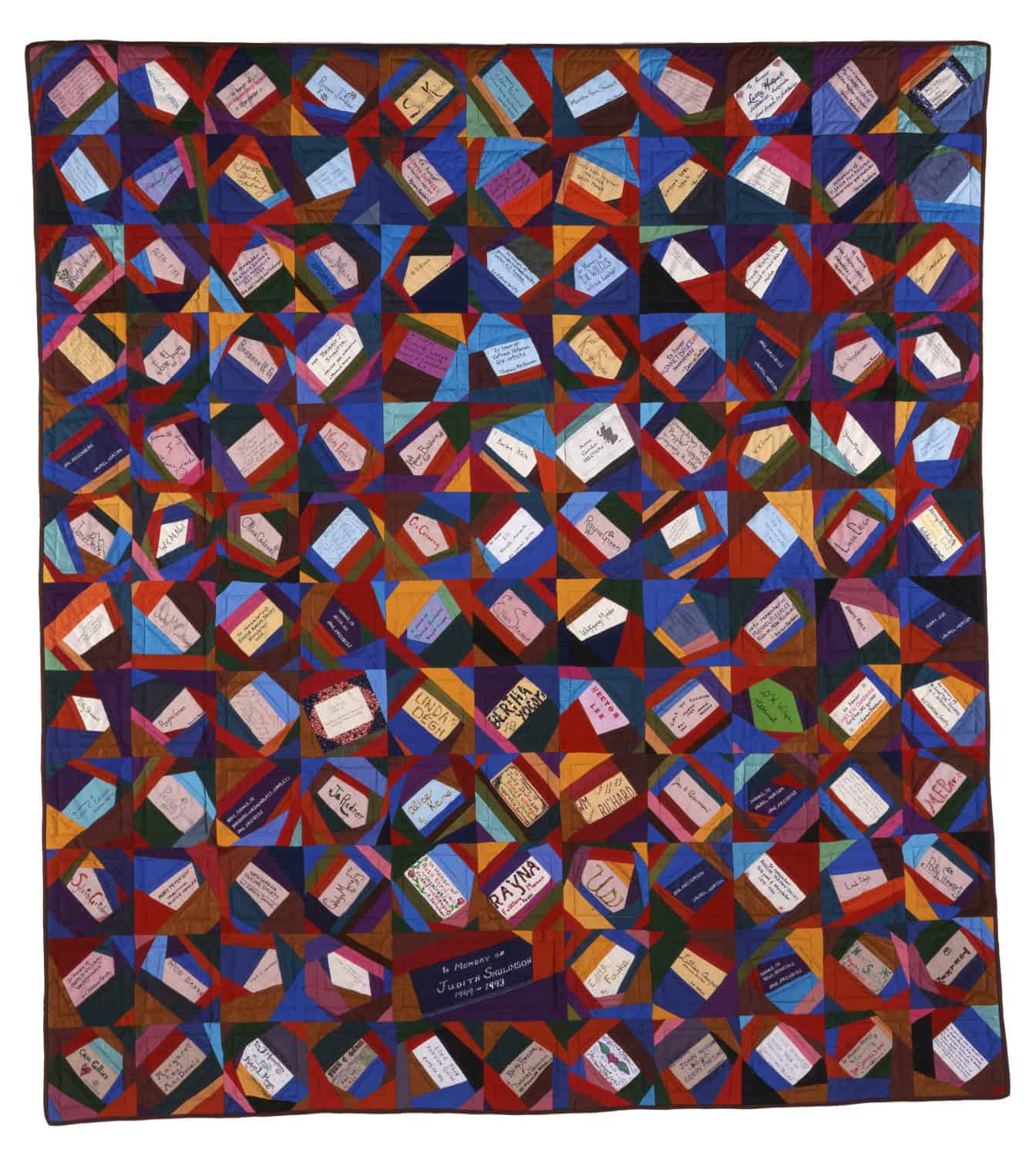 A square quilt made of irregularly shaped, colorful fabric pieces