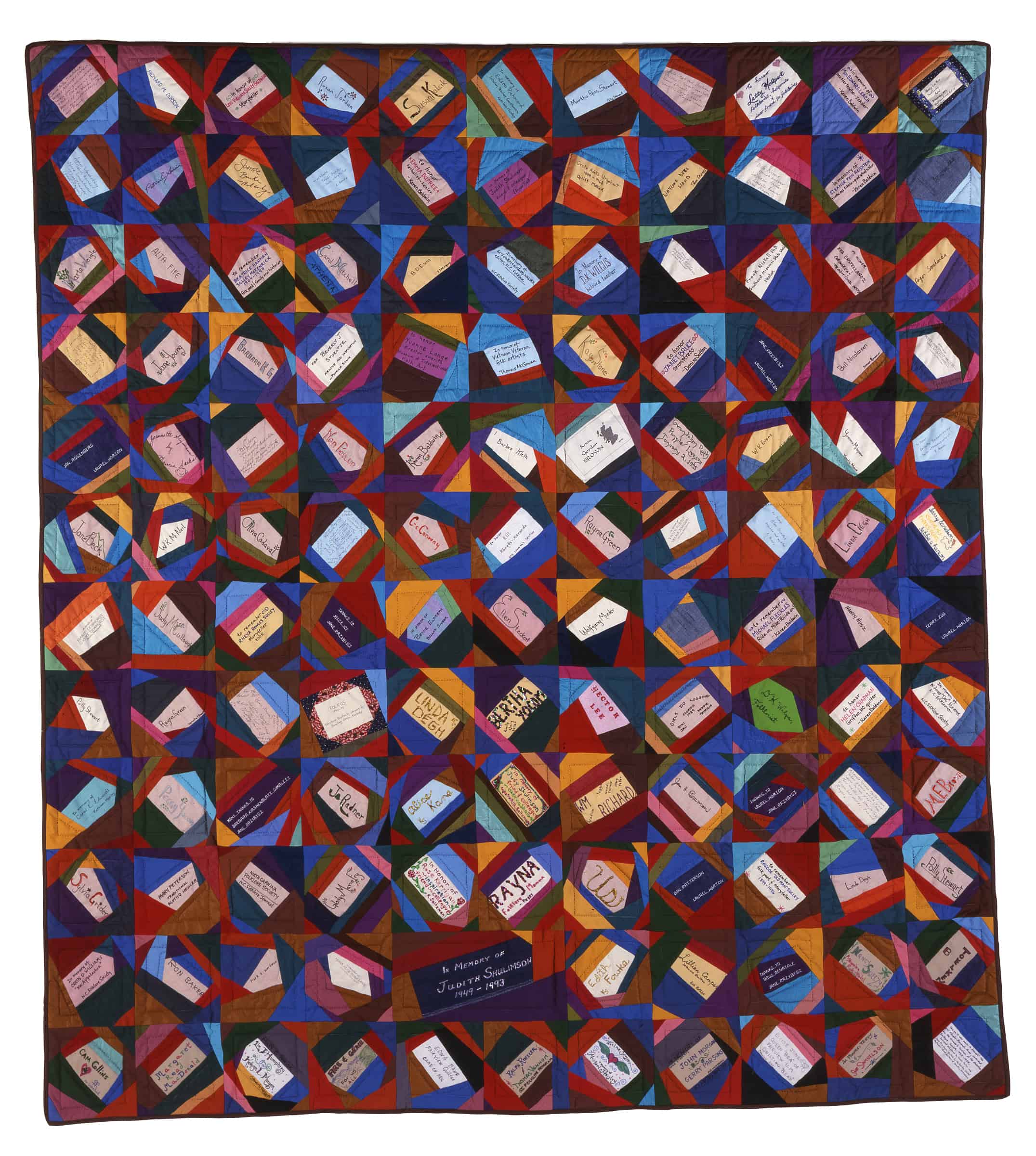 A square quilt made of irregularly shaped, colorful fabric pieces