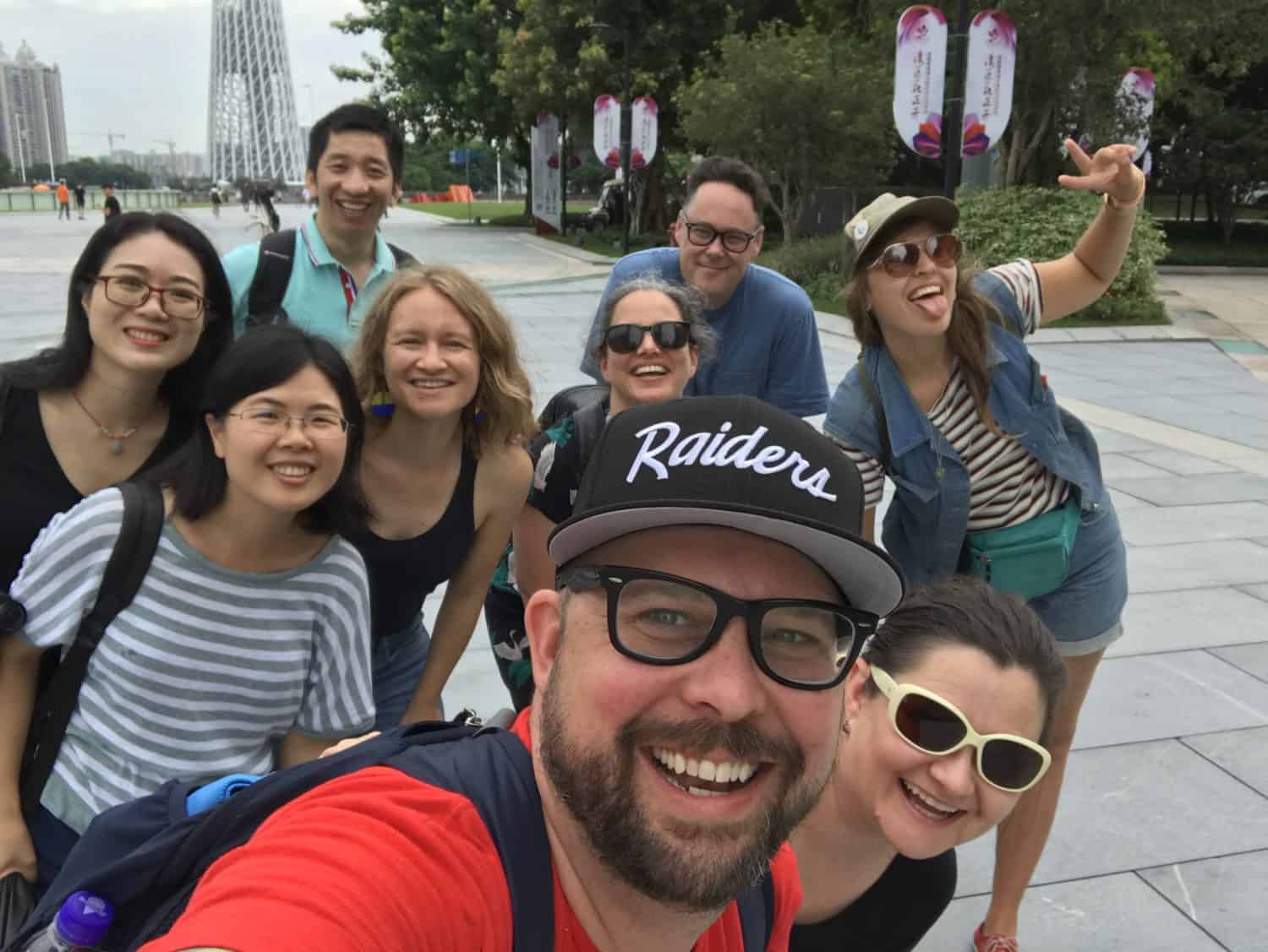 A group of men and women posing for a group selfie, smiling and generally expressing joy towards the camera.