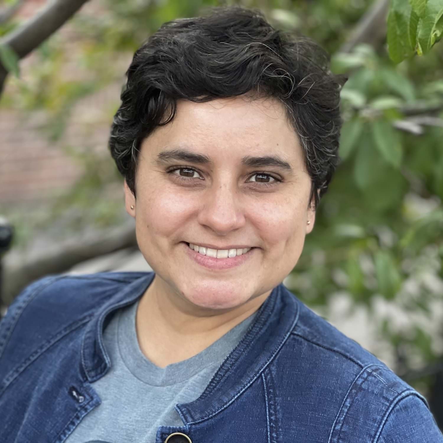 Headshot of Cassie Rosita Patterson smiling, in a blue jacket. Photo credit: Profe Elena Foulis