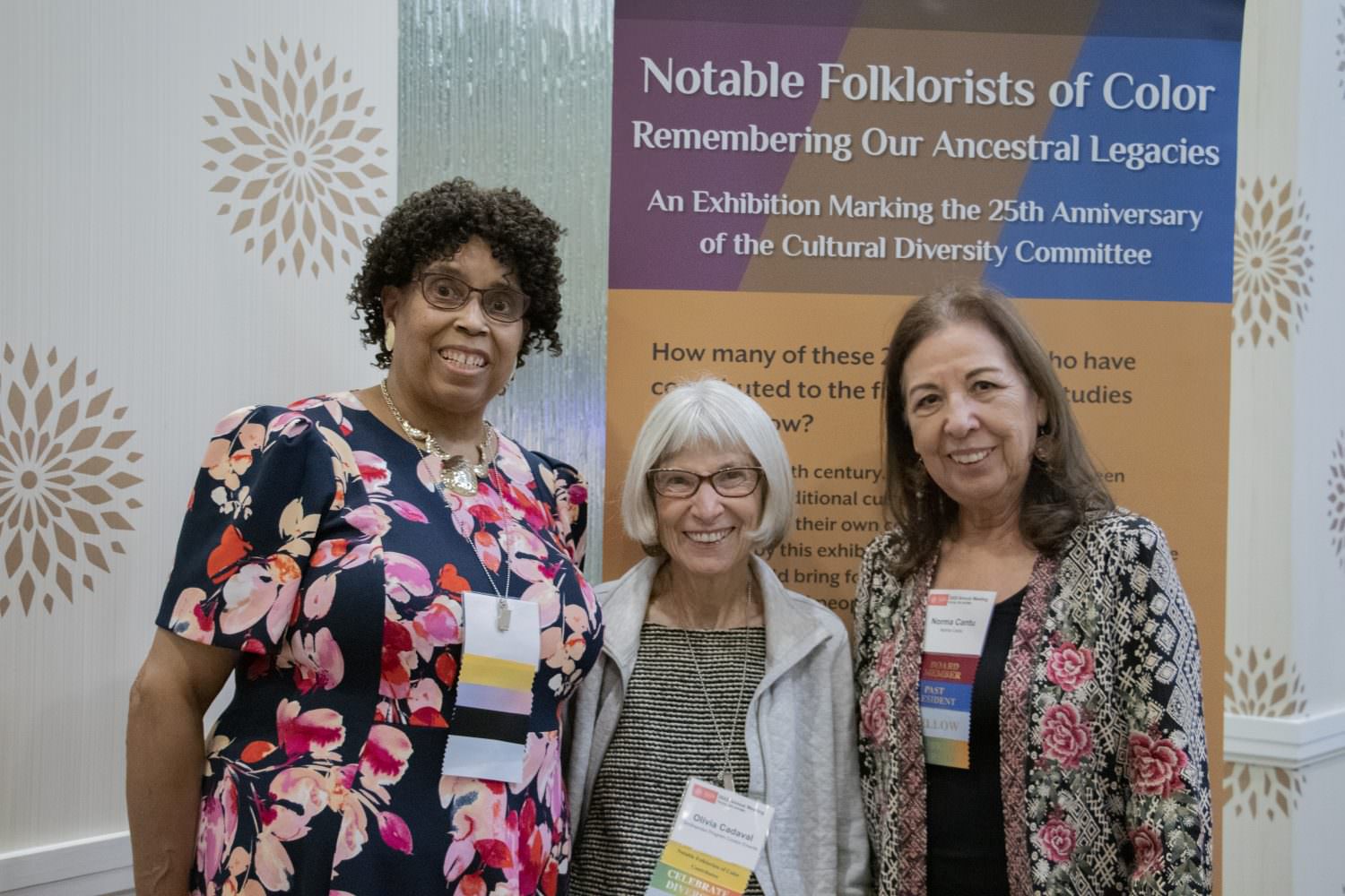 Notable Folklorists of Color curators, Phyllis May-Machunda and Olivia Cadaval with Past President, Norma Cantú standing in front of the exhibition banner
