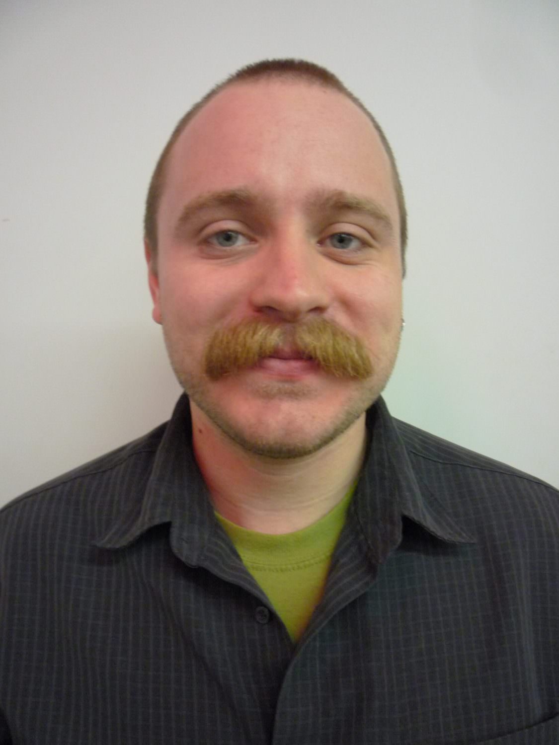 headshot of nicholas miller, who has a mustache and is wearing a grey collared shirt