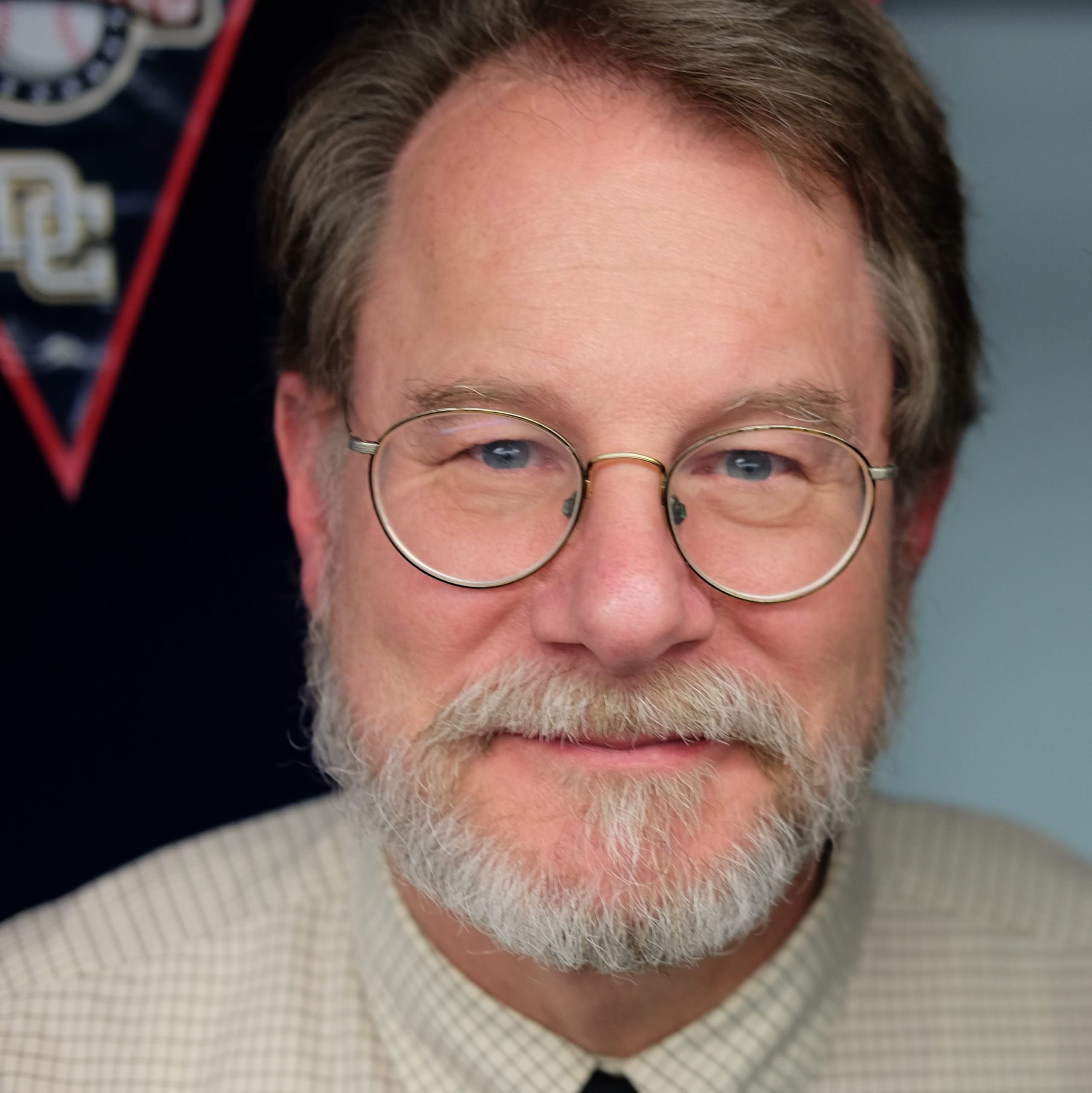headshot of William Mansfield, who wears a tan and blue gingham shirt and wears glasses