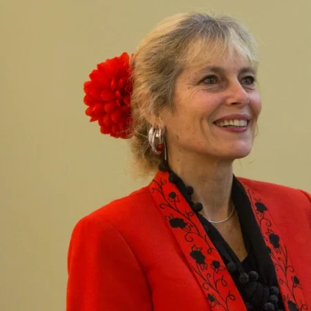 person wearing a bright red jacket with a black collared shirt underneath and a red flower hairtie