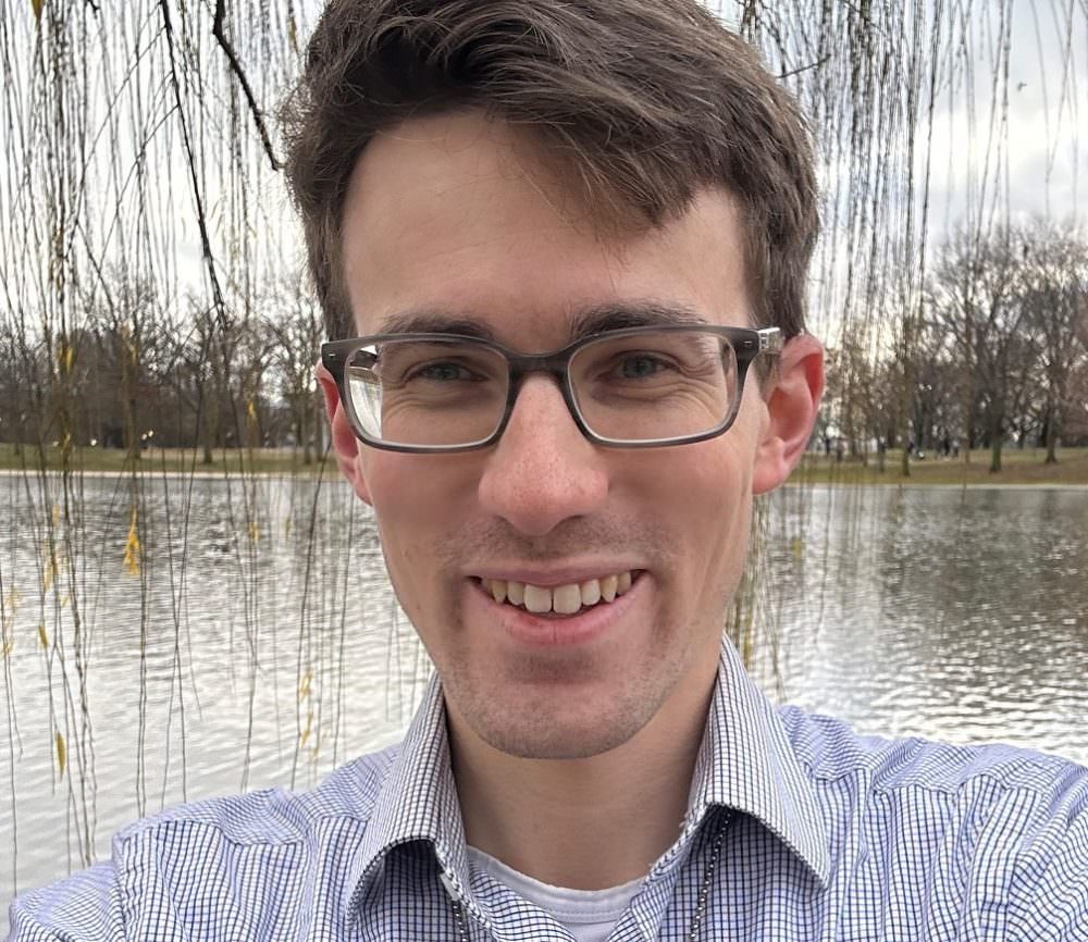 Headshot of Chris Orr from the shoulders up smiling in a dress shirt with a lake and trees in the background.