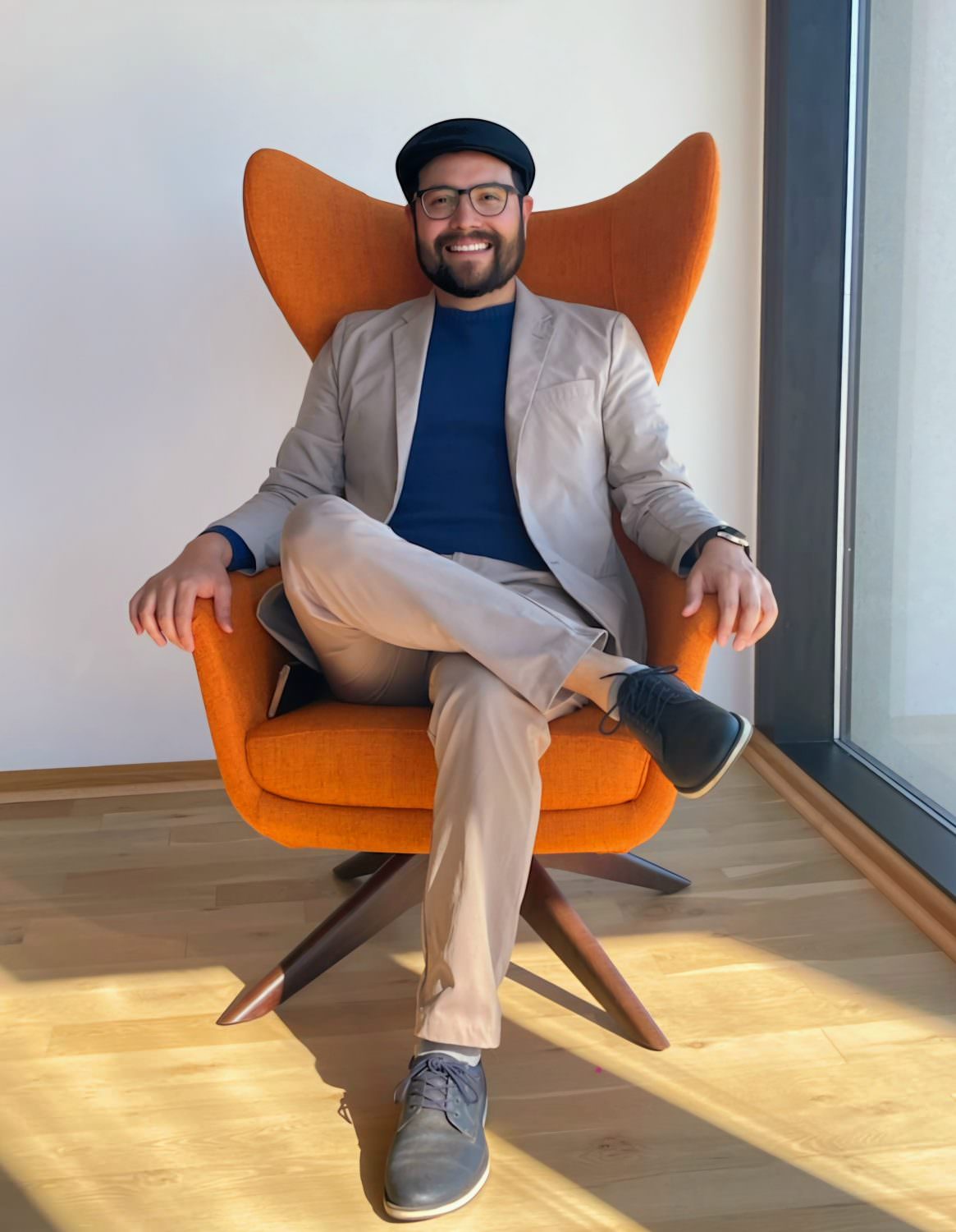 Happy man on an orange chair by a huge window, feeling like a faux CEO