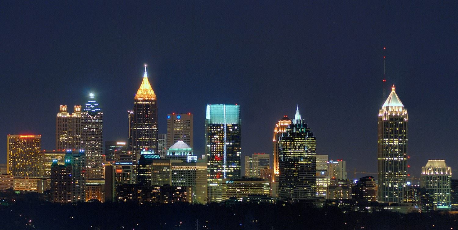 A photo of the skyline of Atlanta at night, showing a row of illuminated tall buildings.