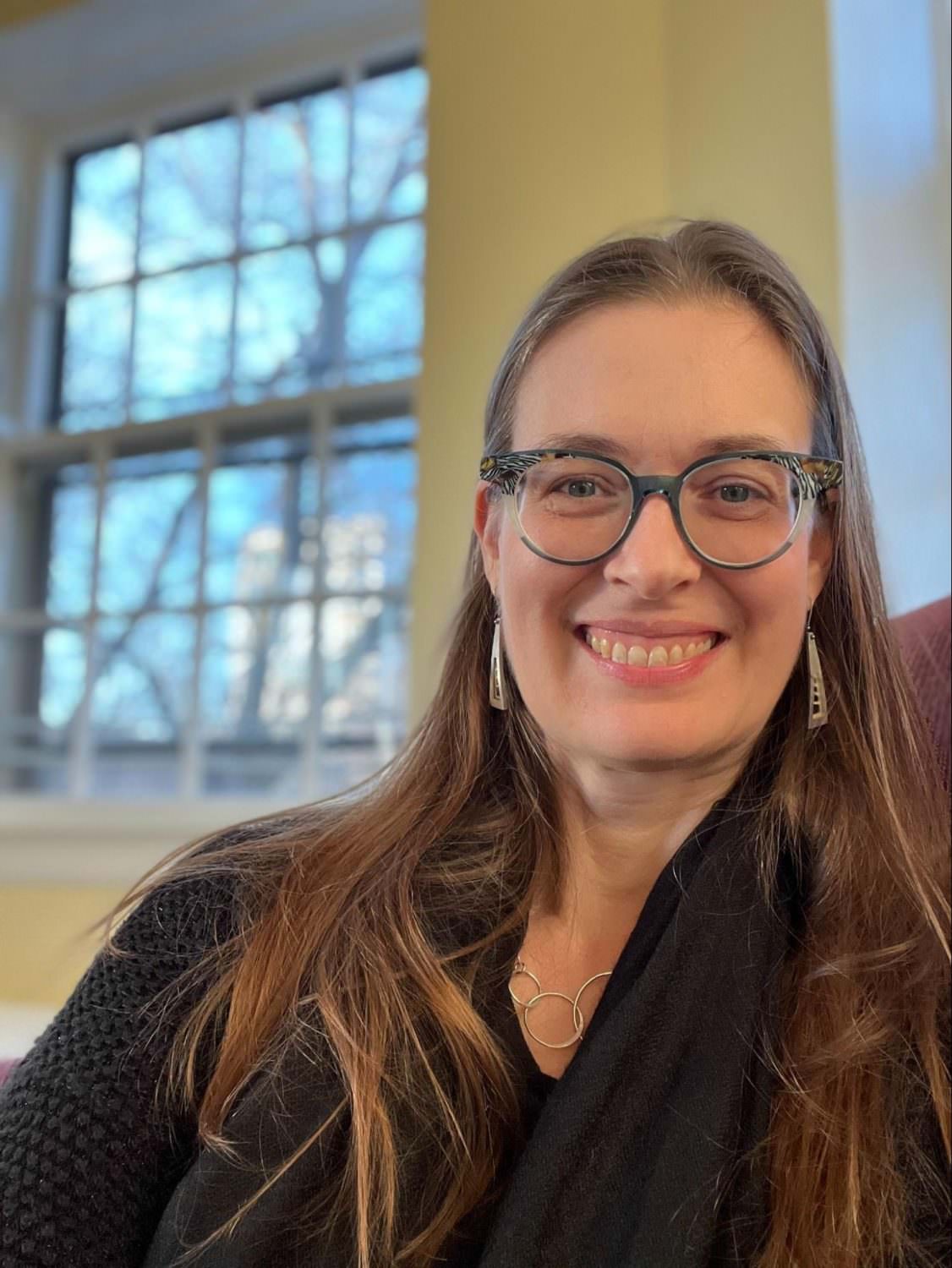 portrait of a female with long hair and a pair of glasses smiling
