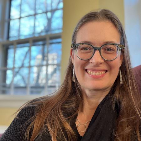 portrait of a female with long hair and a pair of glasses smiling