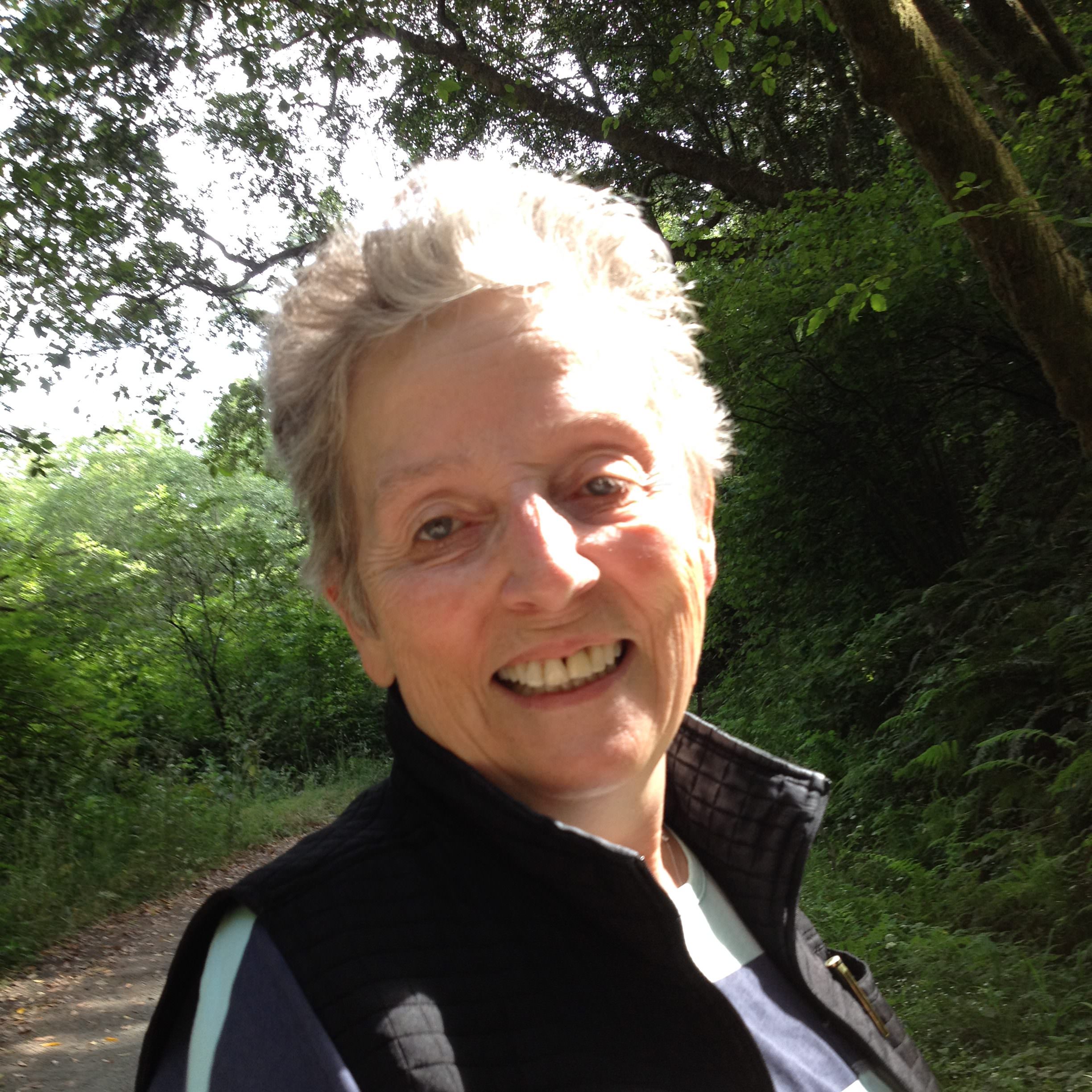 woman smiling and standing on a path in nature wearing a long-sleeve shirt and vest