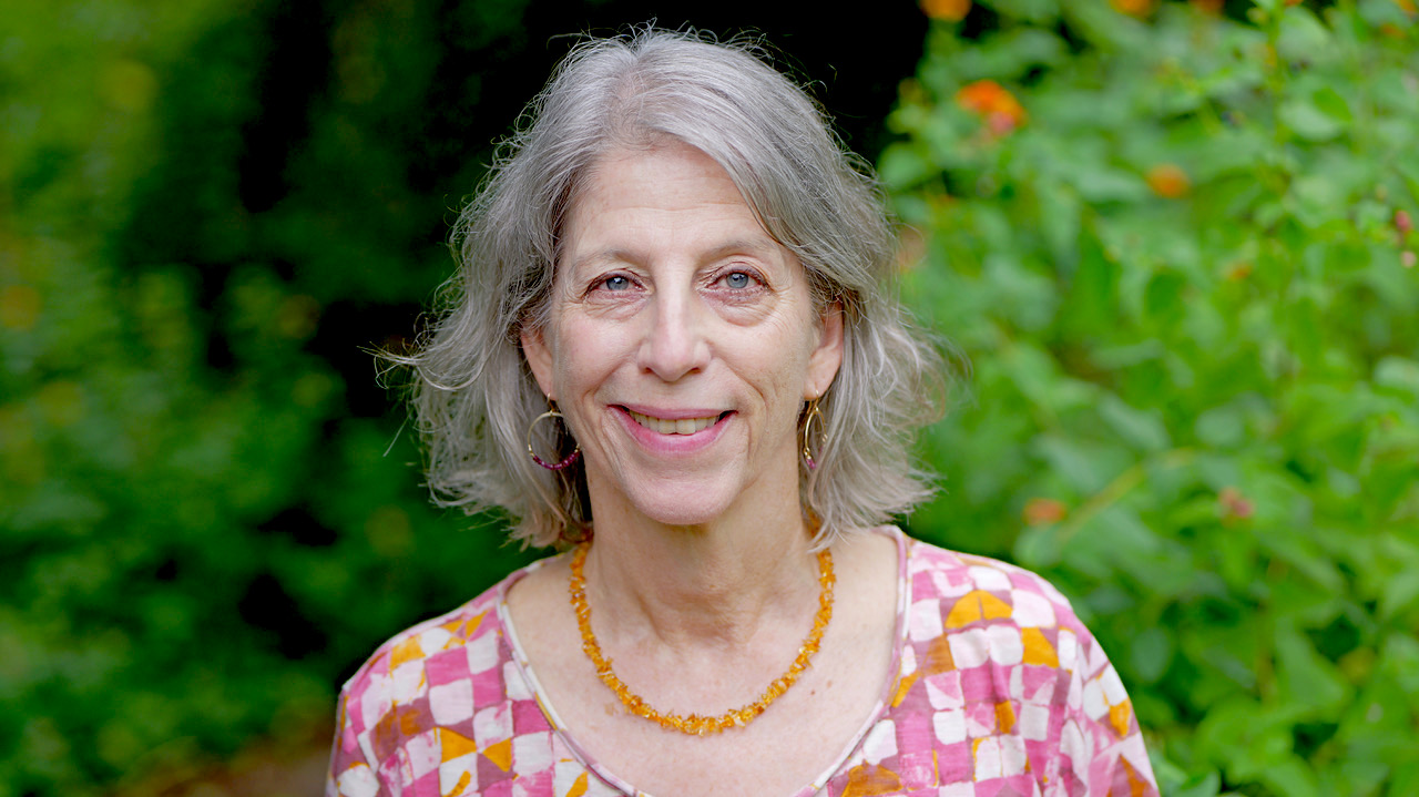 headshot of laura marcus green, who is a white woman with silver hair wearing a quilted pink and orange shirt