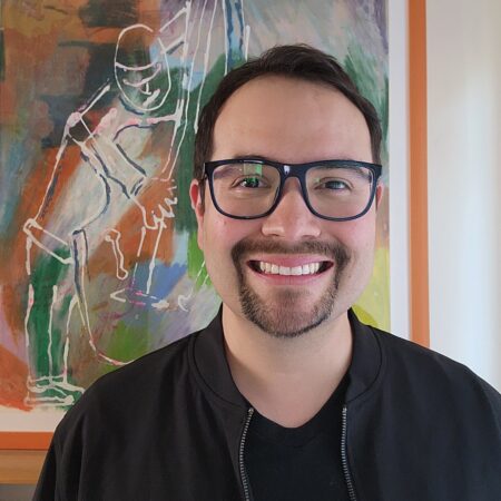 headshot of a smiling male in glasses inside a house