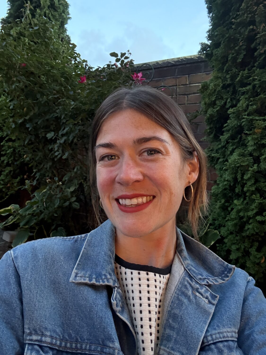 A smiling female in jean jacket standing outside.
