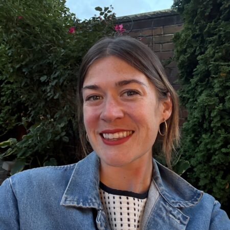 A smiling female in jean jacket standing outside.