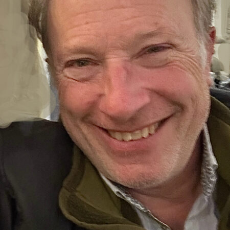 A smiling white male in grey hair in a room