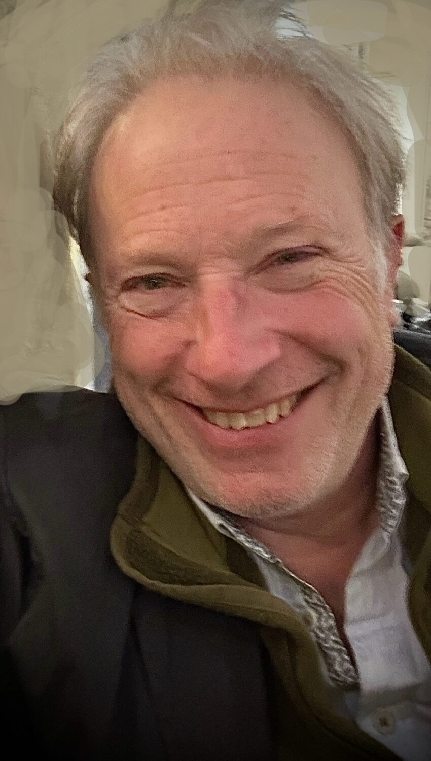 A smiling white male in grey hair in a room