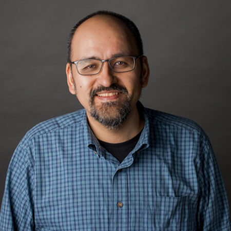 Headshot of a smiling man in glasses and check shirt.