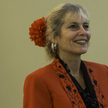 person wearing a bright red jacket with a black collared shirt underneath and a red flower hairtie