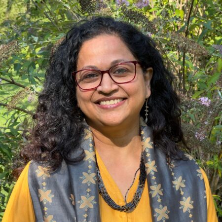 portrait of a smiling Indian woman with curly hair and a pair of glasses