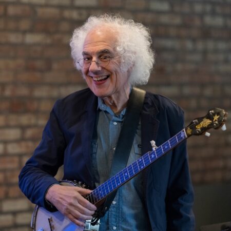 white-haired man in glasses wearing a banjo