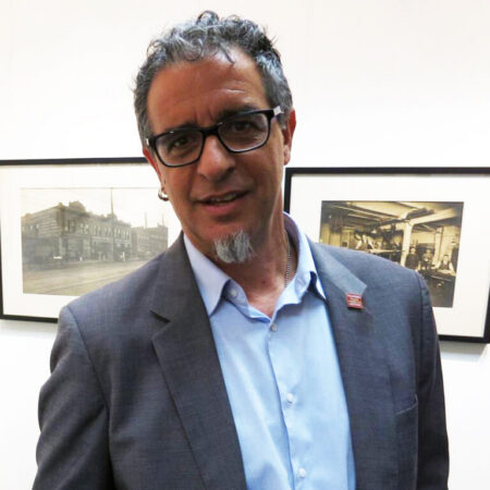 an italian man with glasses, grey hair, and grey beard on his chin; he's also wearing an ear ring on his right ear