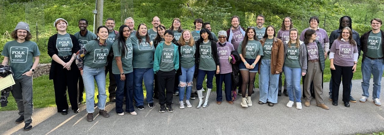 About 30 people who wear t-shirts with "FOLK 100" on them standing together and posing for a photograph